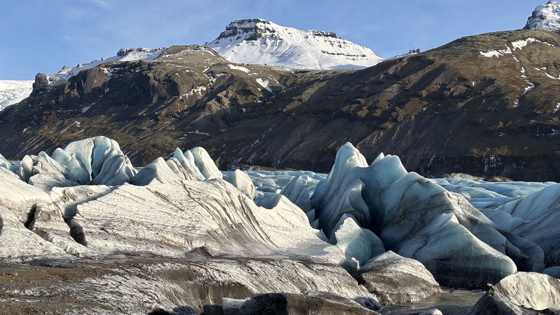 Lengua glaciar de hielo azul y gris descendiendo entre montañas oscuras con cumbres nevadas
