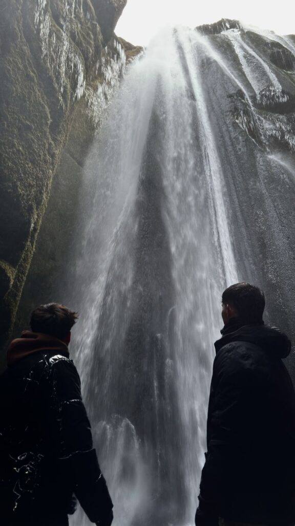 Dos siluetas frente a la cascada de Gljúfrabúi dentro de un estrecho cañón
