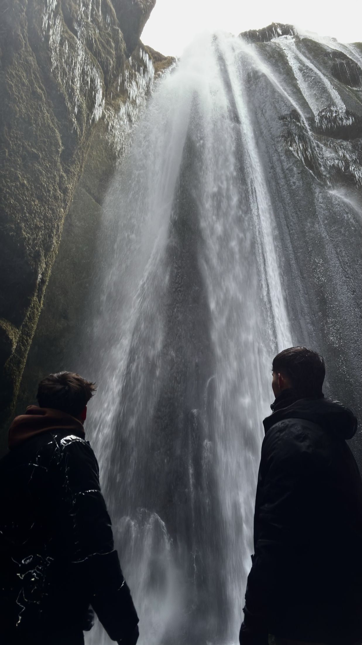 Dos siluetas frente a la cascada de Gljúfrabúi dentro de un estrecho cañón