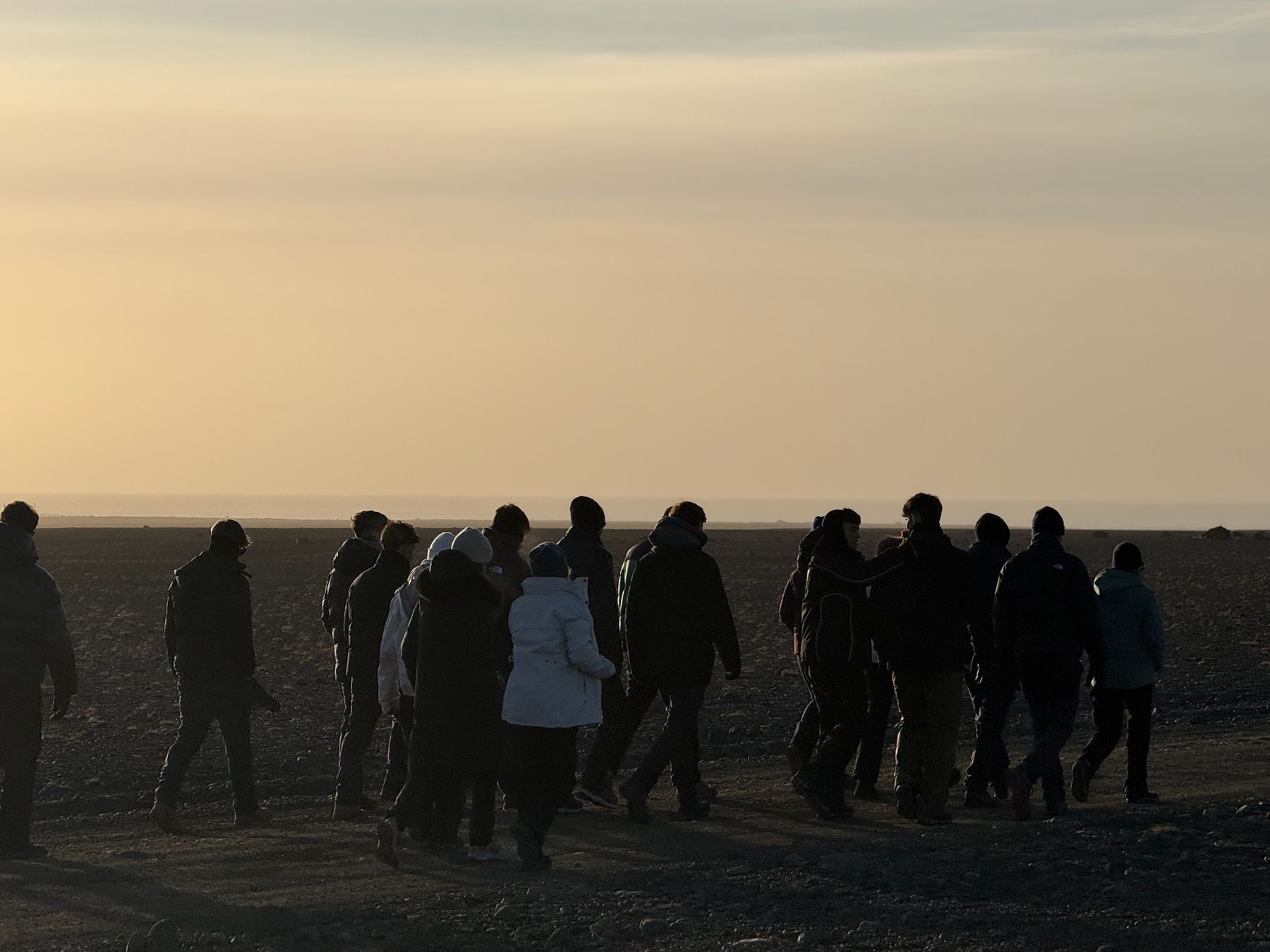 Grupo de viajeros abrigados caminando a contraluz por una llanura al atardecer