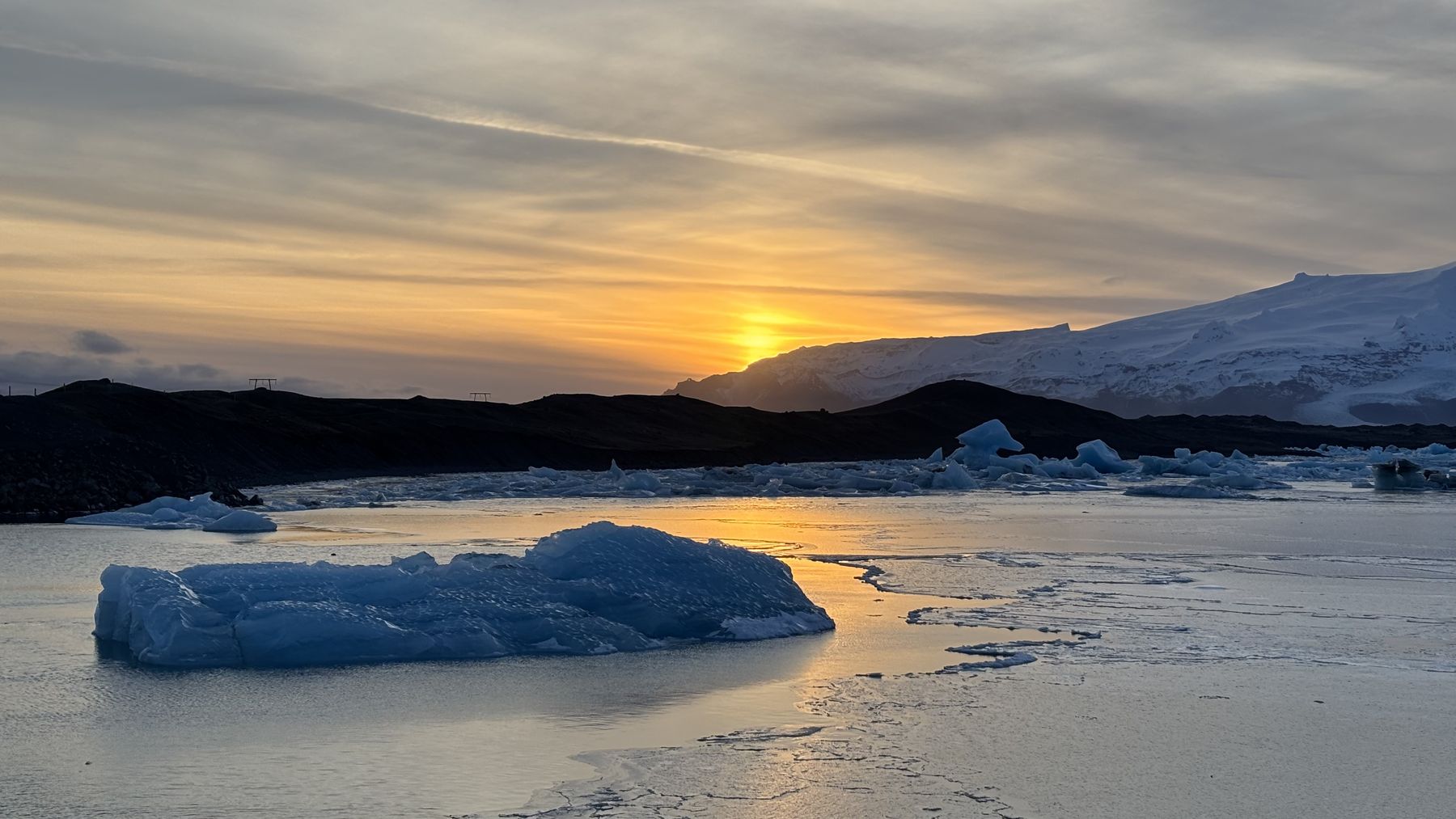 Iceberg azul flotando en la laguna de Jökulsárlón con el sol bajo reflejado en el agua