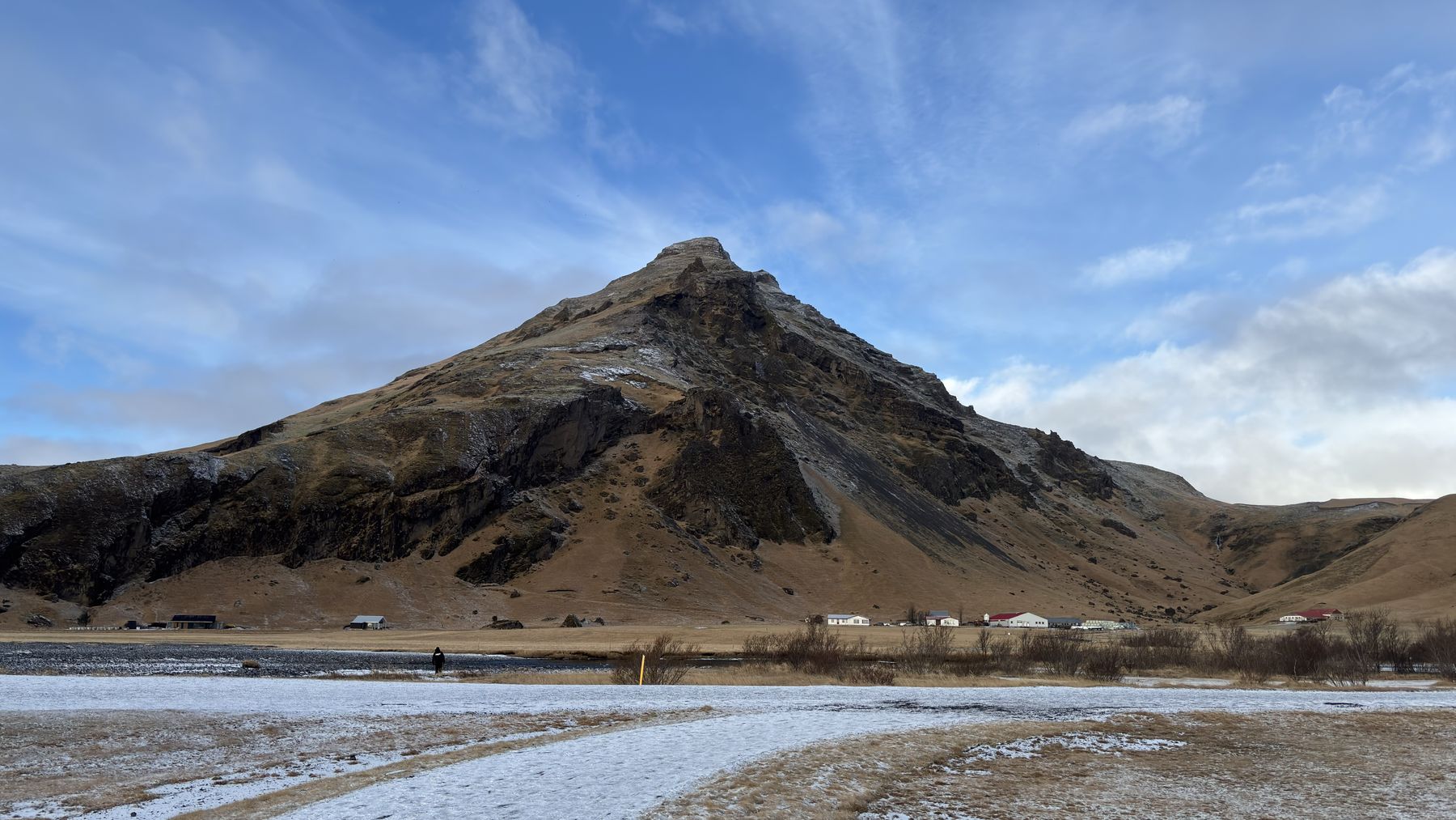 Montaña volcánica de laderas oscuras con nieve en la base bajo un cielo azul