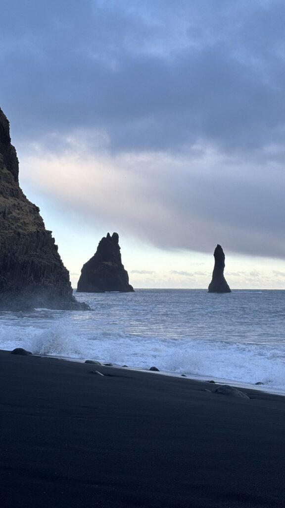 Olas rompiendo en la orilla negra de Reynisfjara con los farallones al fondo